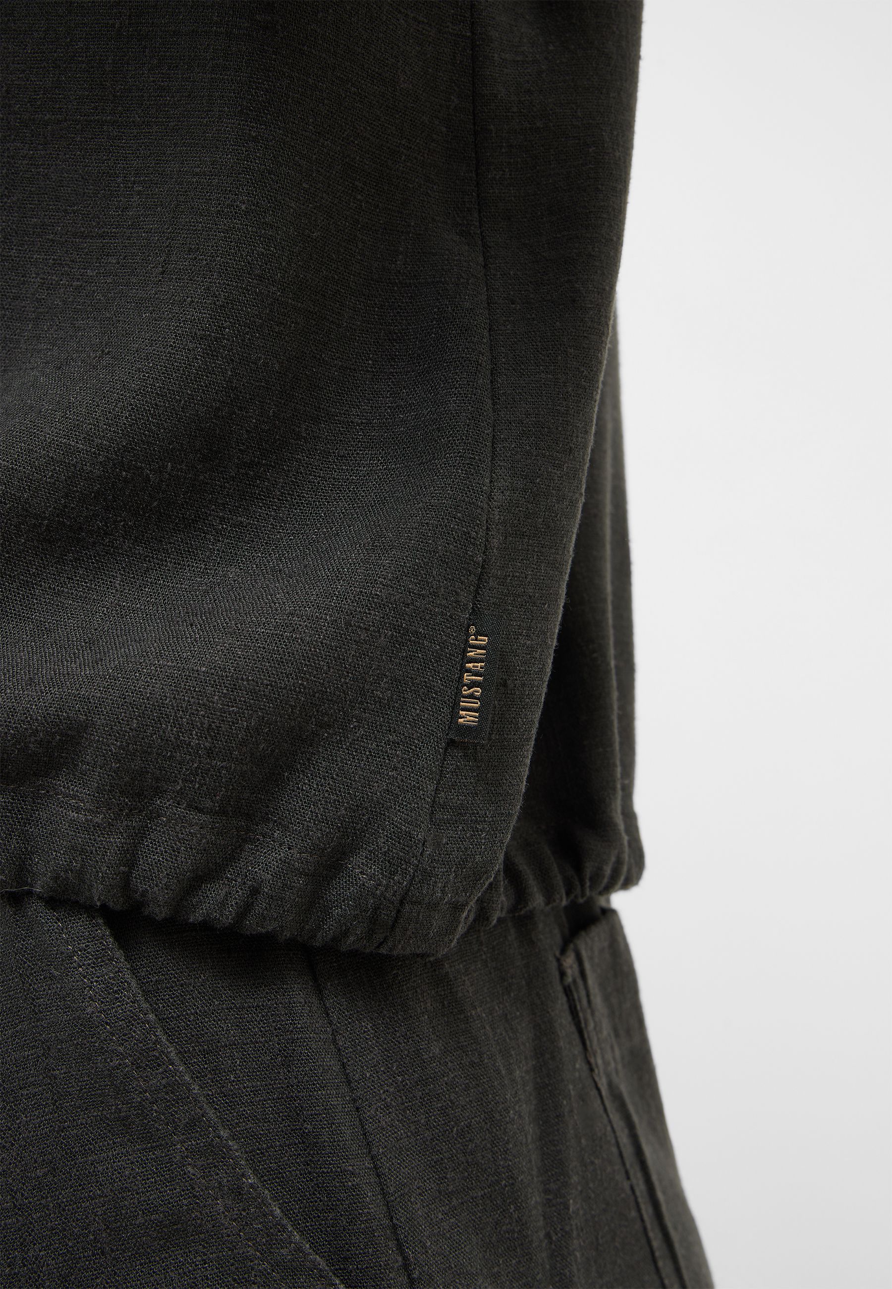 schwarzer Stoff, Bekleidungsdetail, Reißverschluss-Label, Mustard-Brand-Tag, Knöchelnaht